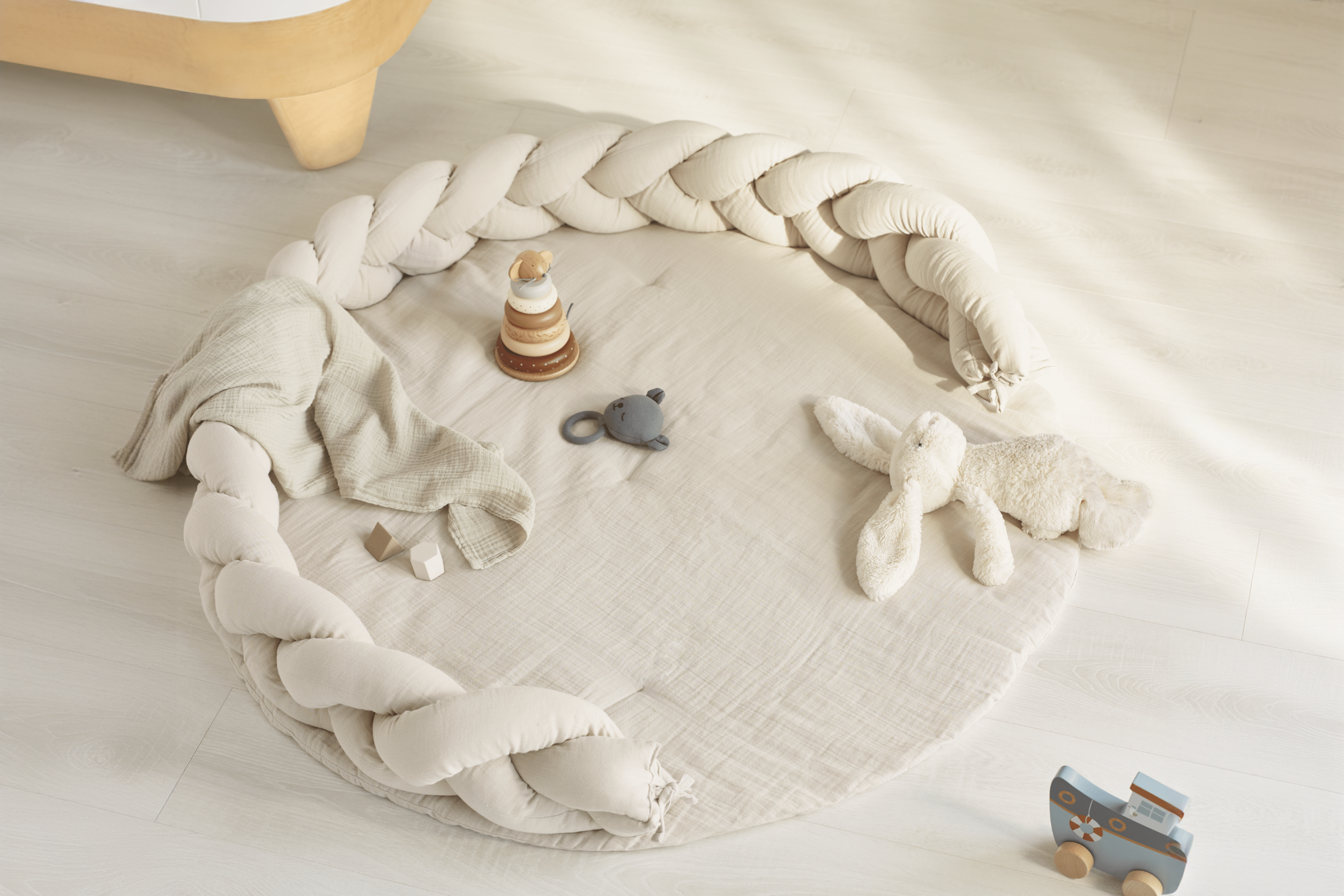 This image shows the Maia Muslin Playmat surrounded by the Braided Pillow and little toys scattered across it