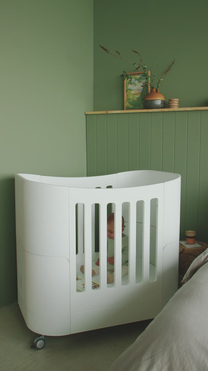 Video of a mother lifting her baby from the mini cot and showing how the cot wheels work